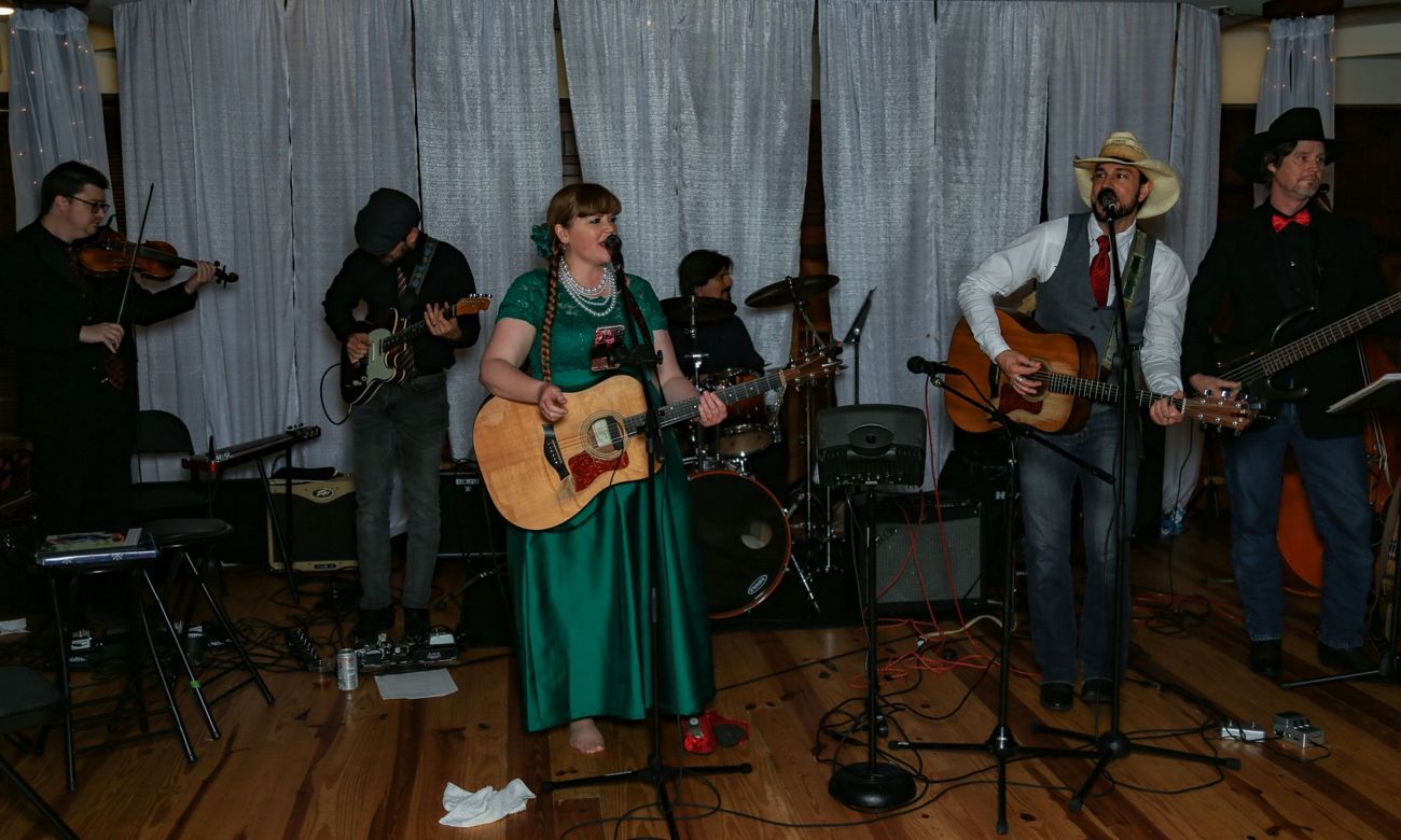 A full band with fiddle, guitars and a singer in a green dress