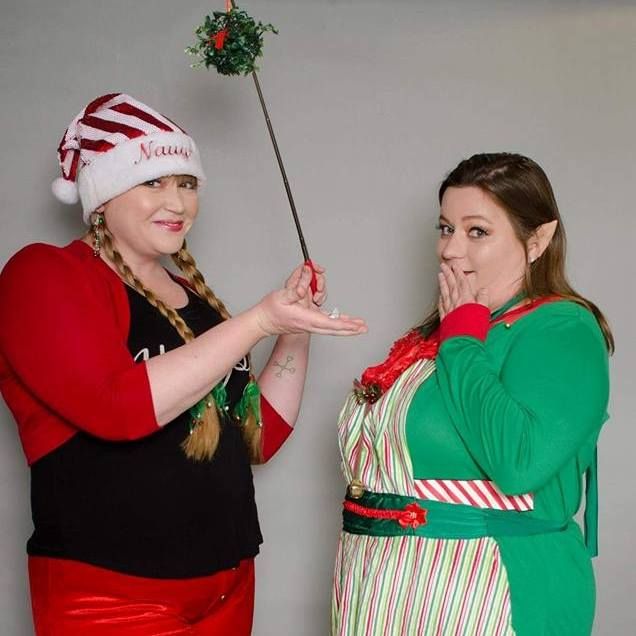 Two women dressed as Christmas elves, one holding up mistletoe