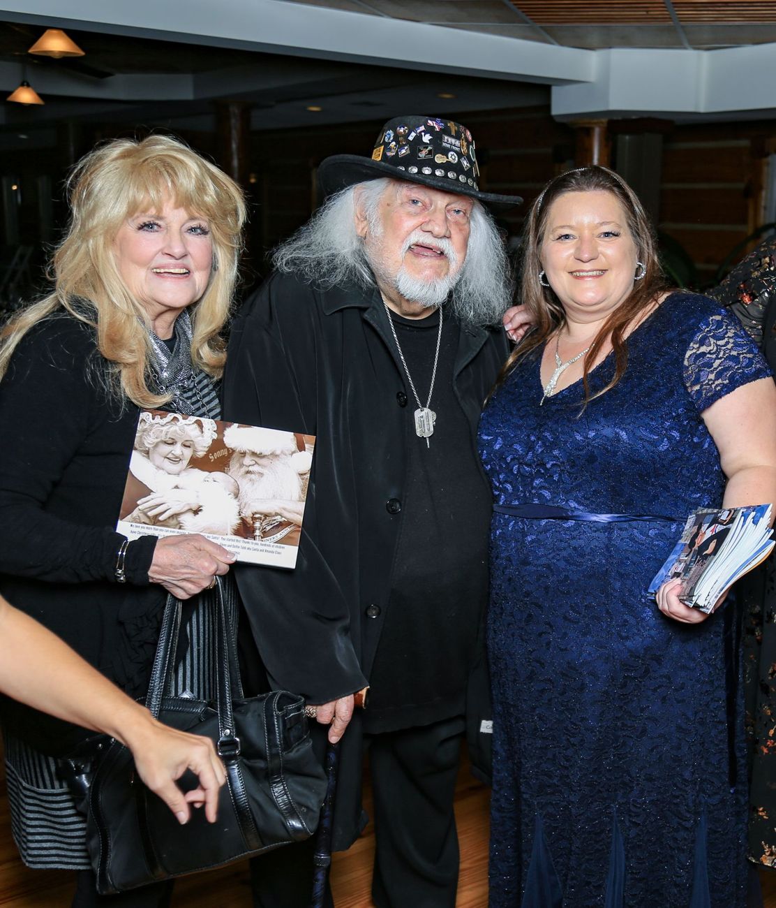 Three friends at a Christmas gala, one holding a framed photograph