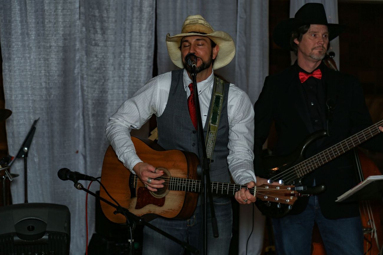 Two musicians on stage, one in a cowboy hat singing with an acoustic guitar