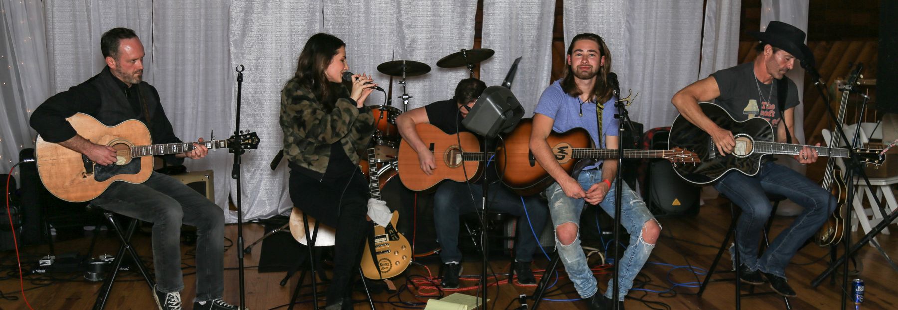 Five musicians with acoustic guitars playing a songwriters' round